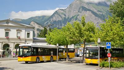 Bahnhof Bad Ragaz im Sommer mit drei Postautos, welche alle zeitnah abfahren.