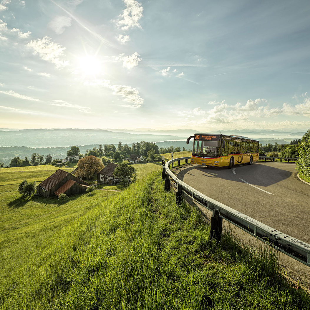 A Postbus travels over the Albis Pass towards Hausen am Albis, Post. Lake Zurich can be seen in the background.
