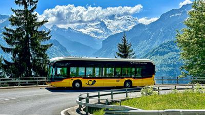 Elektro-Postauto in Kurve mit Bergpanorama im Hintergrund