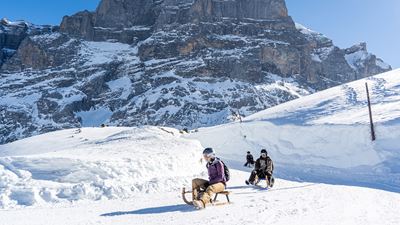 Three sledgers in a row on Davos sledges in front of a sheer rock face hurtling towards Schwarzwaldalp.