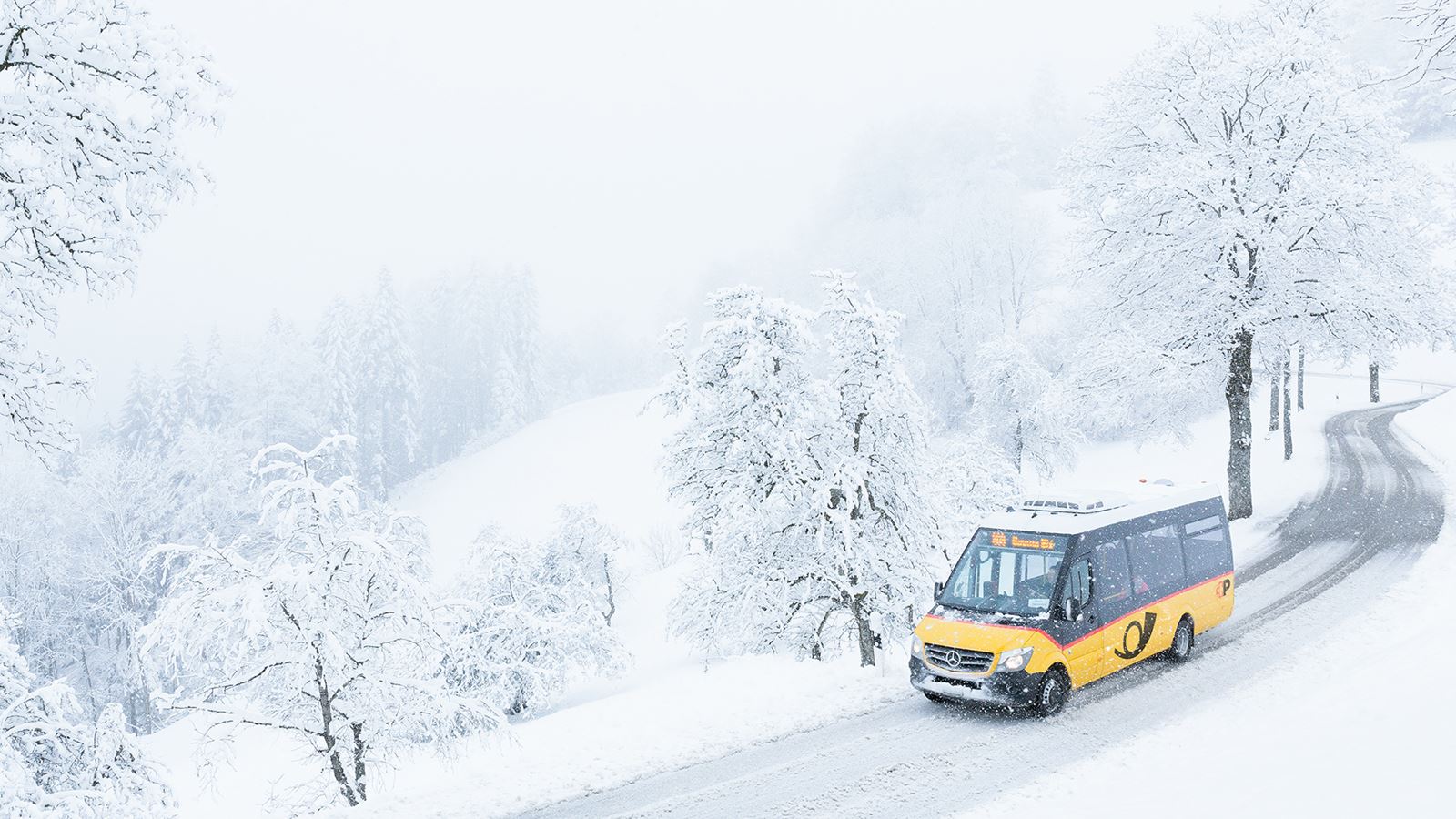 A small Postbus driving through the snowy streets of Sternenberg
