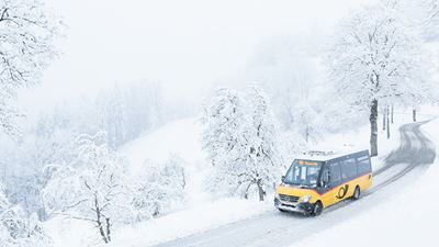 Ein kleines Postauto fährt durch die verschneiten Strassen von Sternenberg
