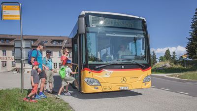 Familie mit Kindern steigt an einer Bushaltestelle ins Postauto