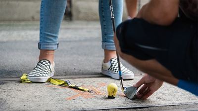 Primo piano di piedi e gambe con pallina gialla e racchetta sul percorso dell’Urban Golf a Winterthur.