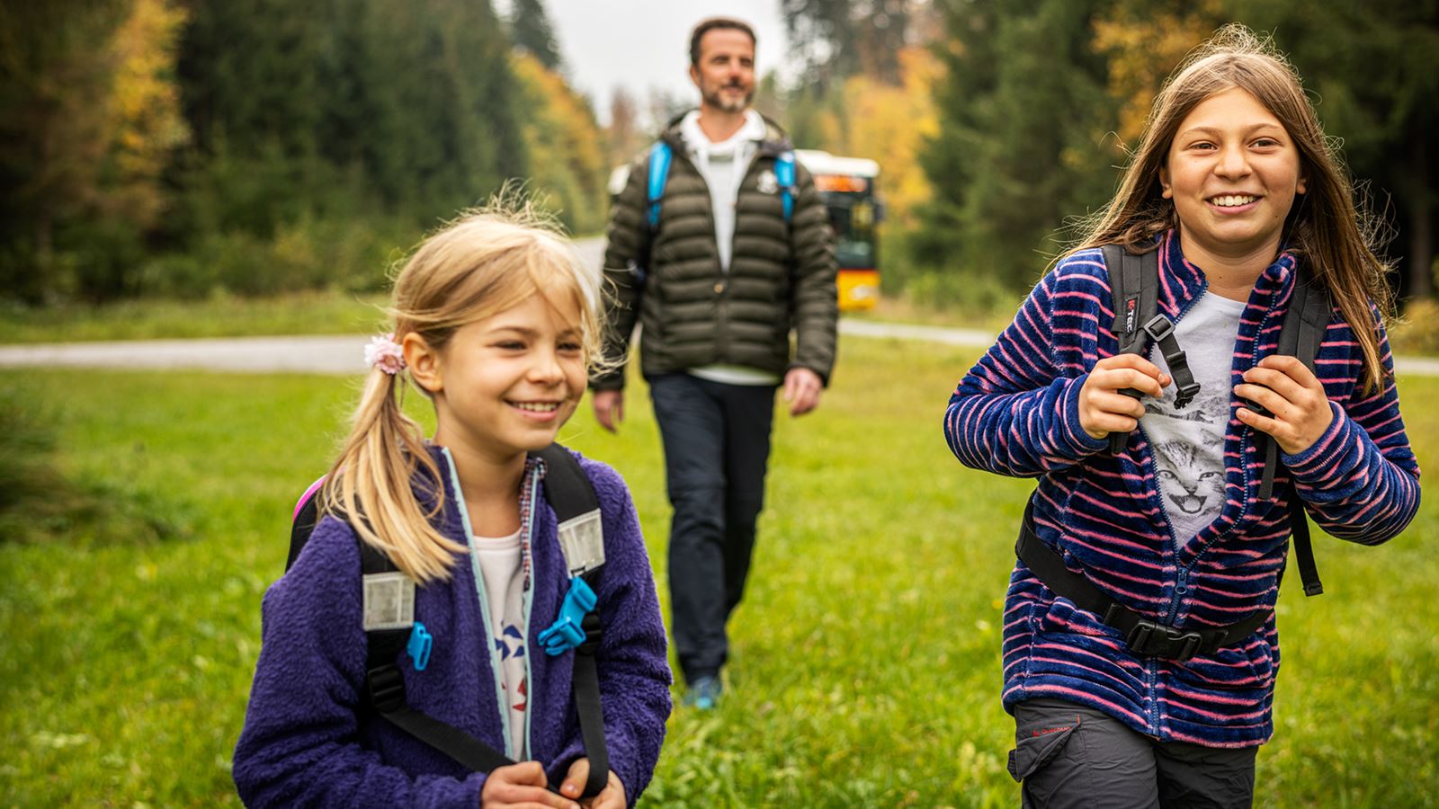 Eine Person steht auf einem Feld. Die Person trägt einen runden Stohhut, einen pinken Rucksack und ein blau-rotes Flanell Hemd und blaue Jeans.