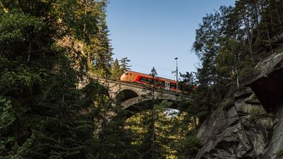 SOB train on a stone bridge in the middle of a wooded valley in a clear sky.