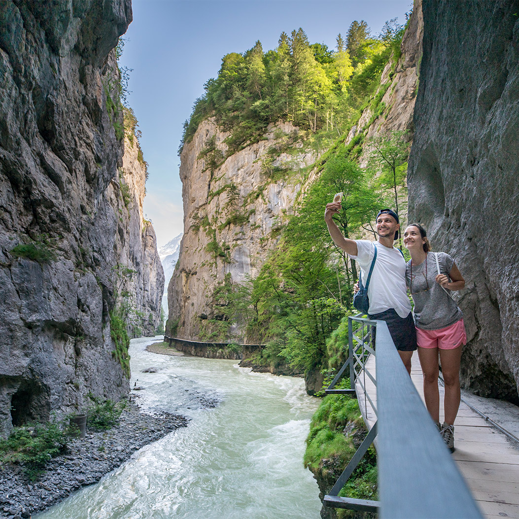Zwei Wanderer stehen auf einem schmalen Steg entlang einer Aareschlucht und machen ein Selfie.