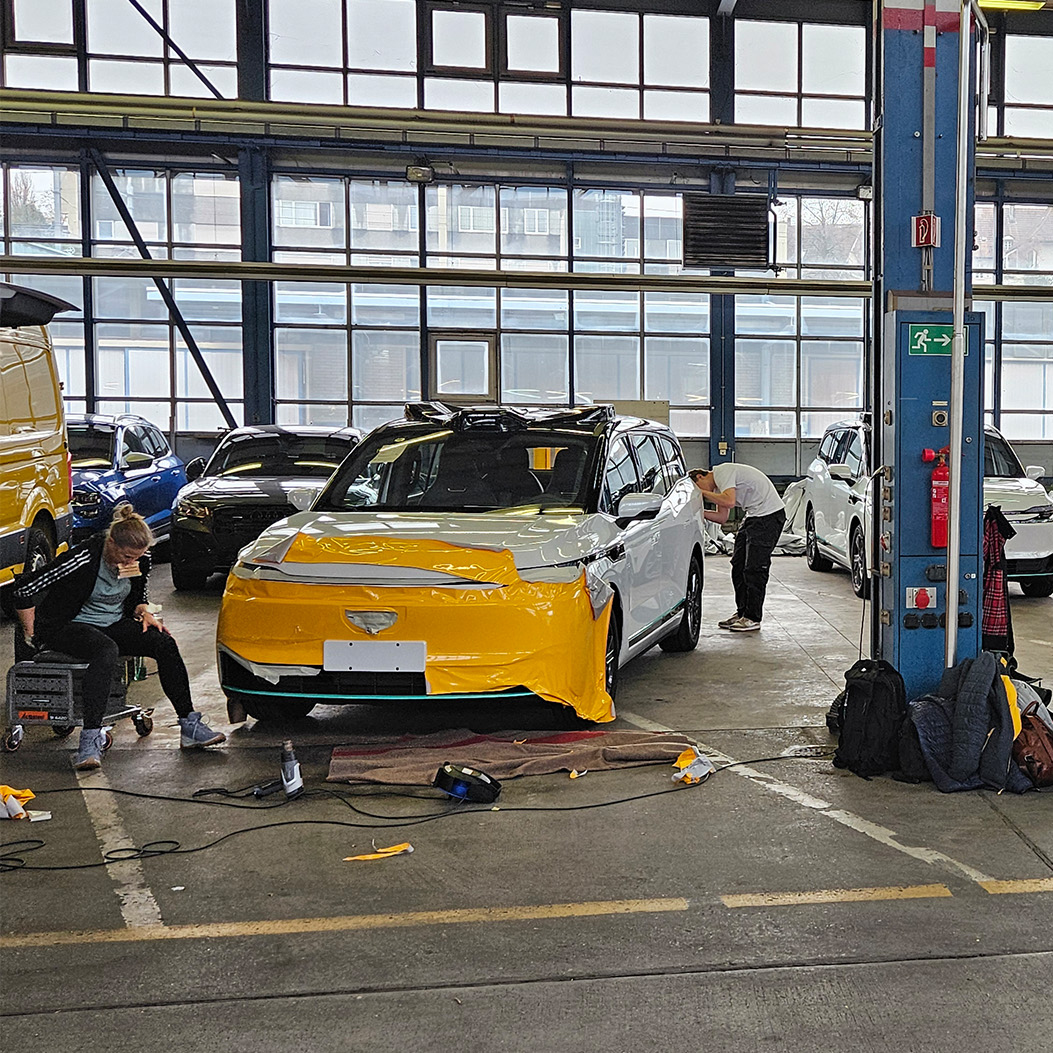 Several Swiss Post AmiGo autonomous vehicles are being film-wrapped with the post horn in a factory hall.