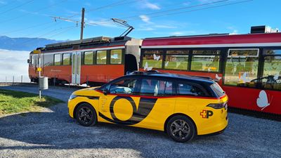 AmiGo vehicle is standing next to a train on a rural railway line.