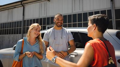 Three people meet in front of a car to commute to their workplace together. 