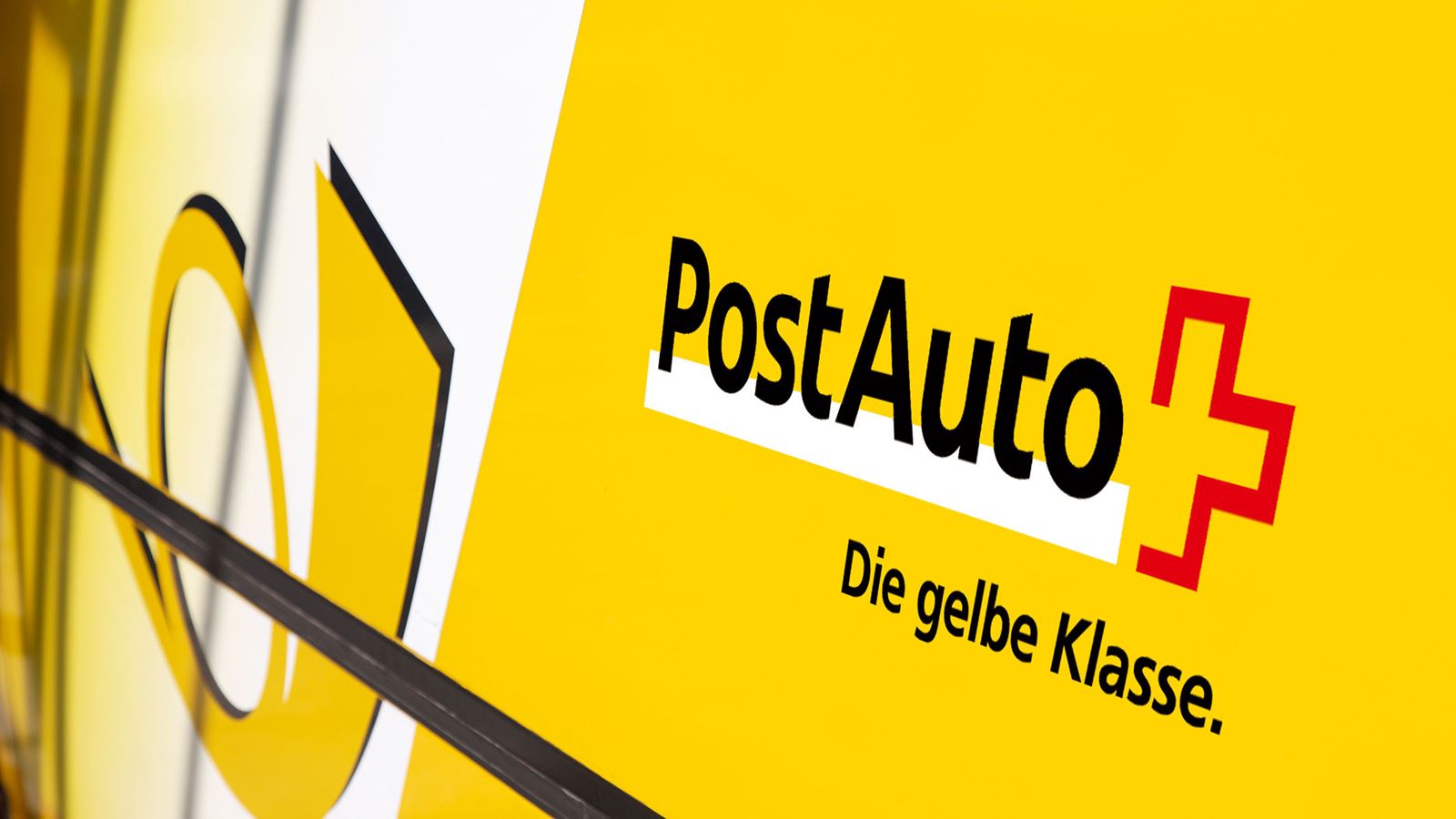 A close-up of a Postbus that shows the company name, the post horn and the claim “The yellow class”. 