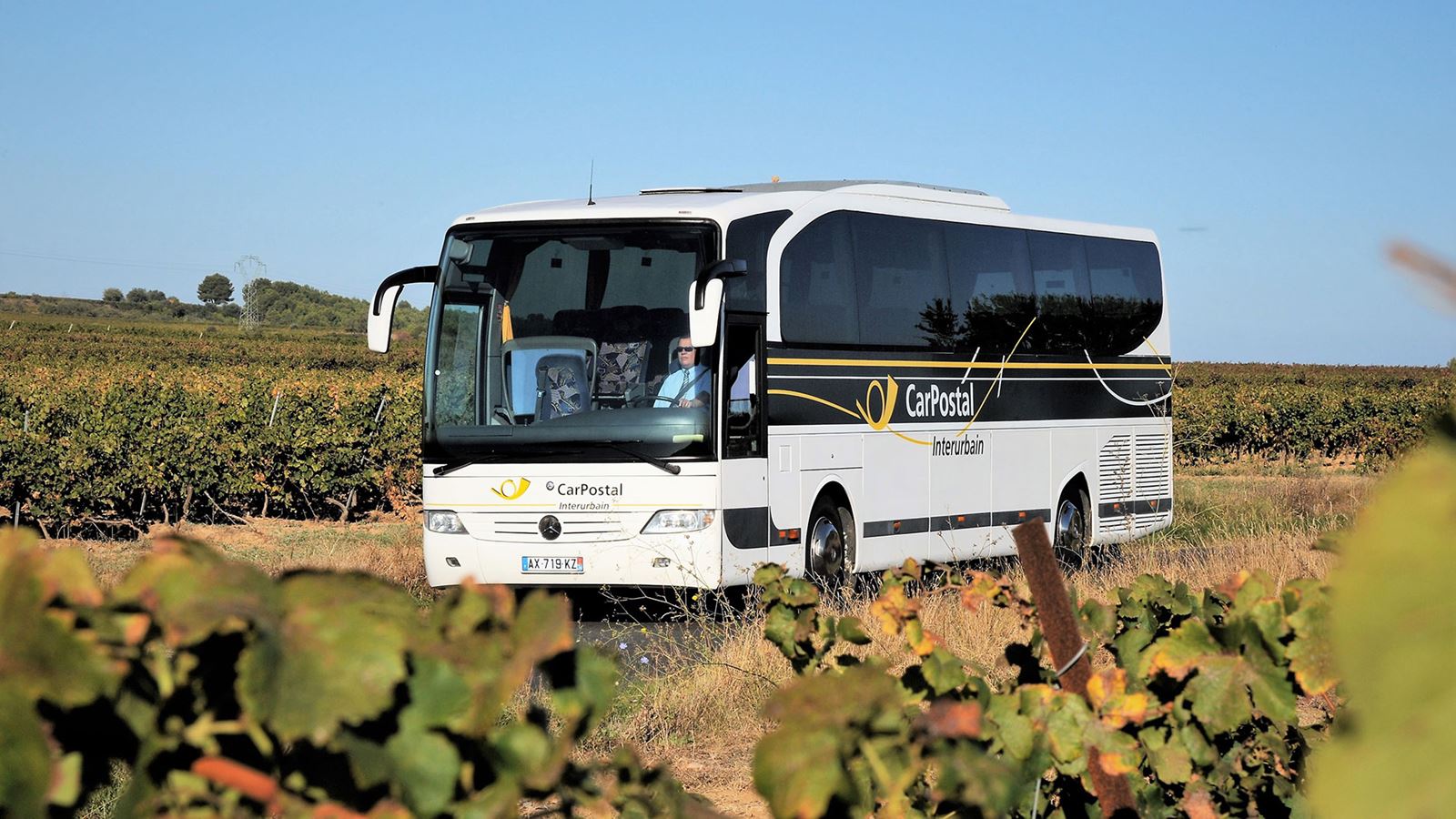 The image shows a white CarPostal vehicle on a road in France. 