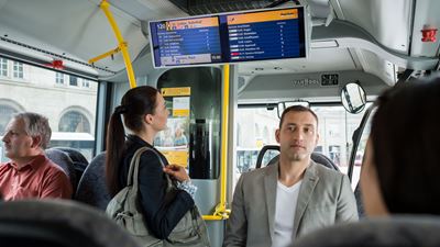 A passenger looks up information on a Postbus screen display.