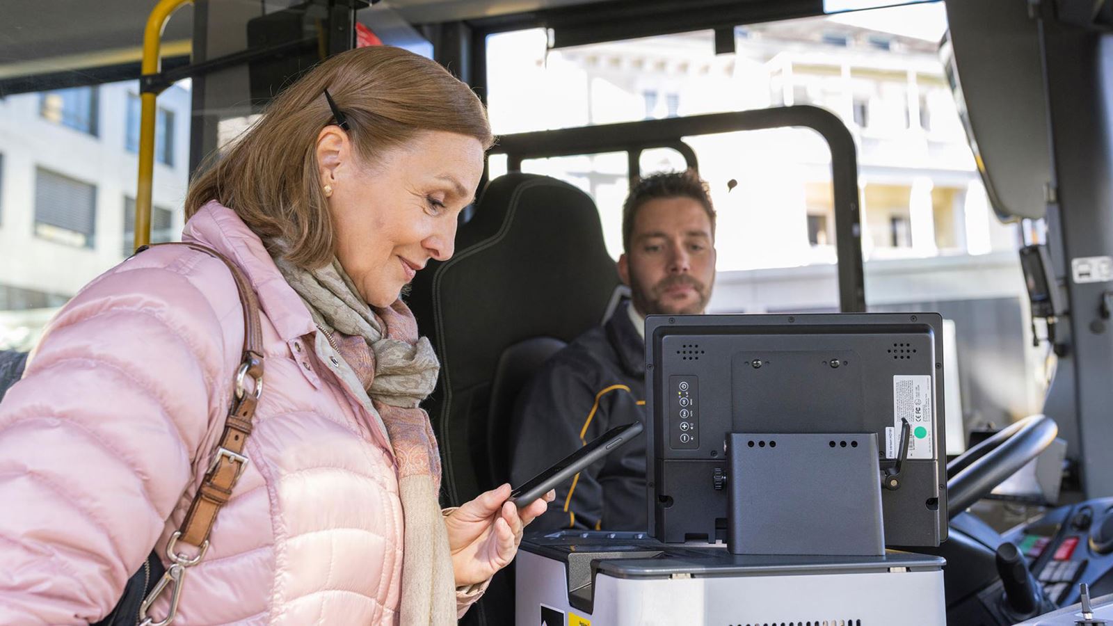 Une femme achète son billet en montant dans le CarPostal. Elle regarde son smartphone.