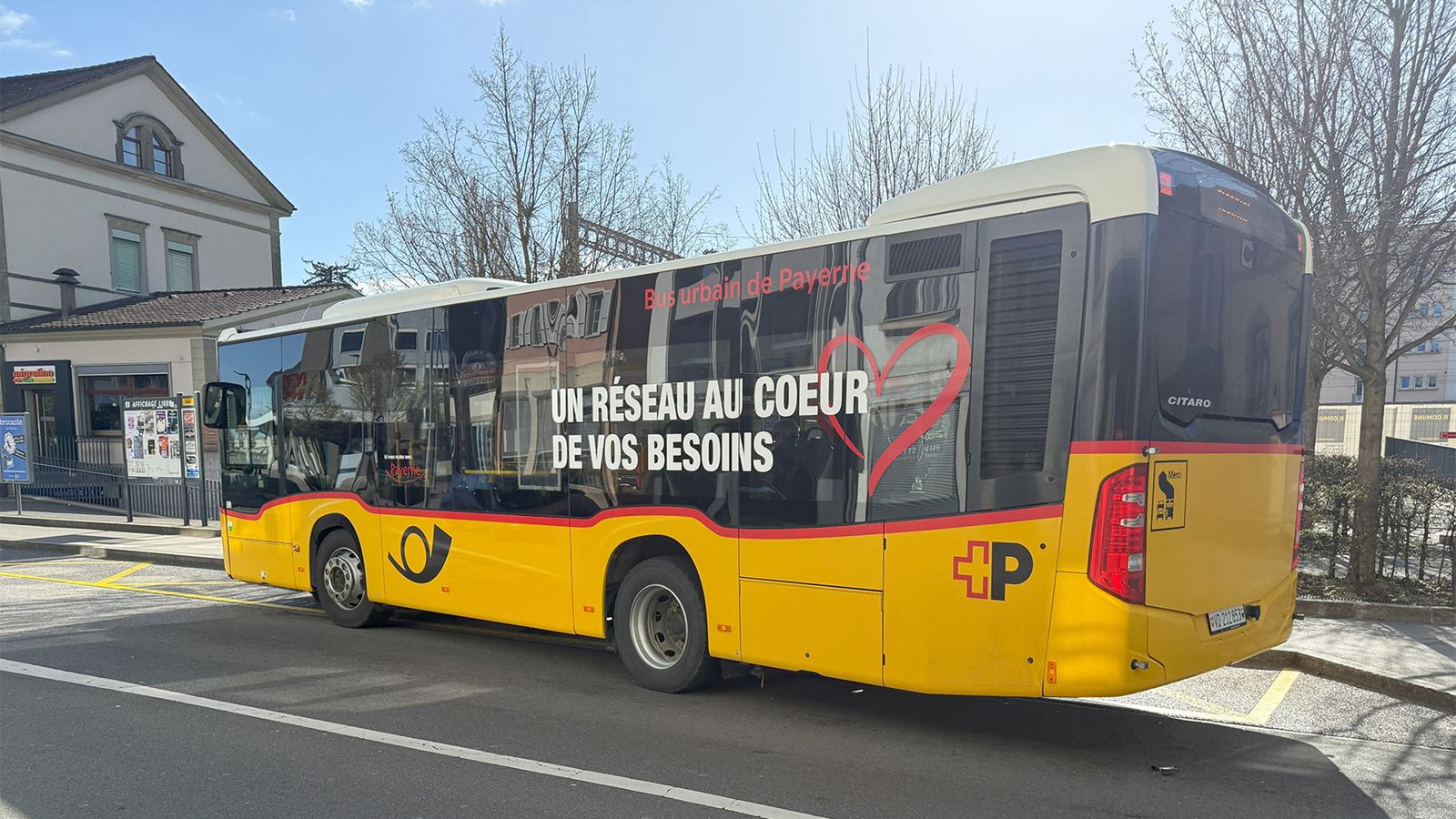 A Payerne PostBus local bus parked in front of a railway station