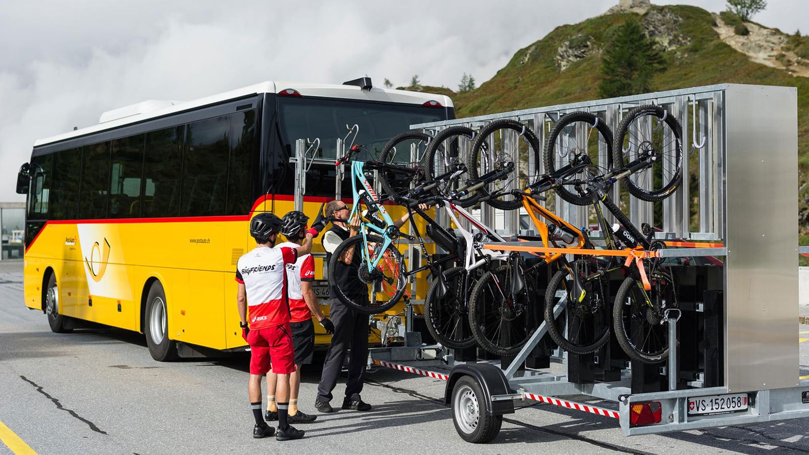 La photo montre deux personnes qui hissent leur vélo sur une remorque. Un chauffeur les aide dans cette démarche.