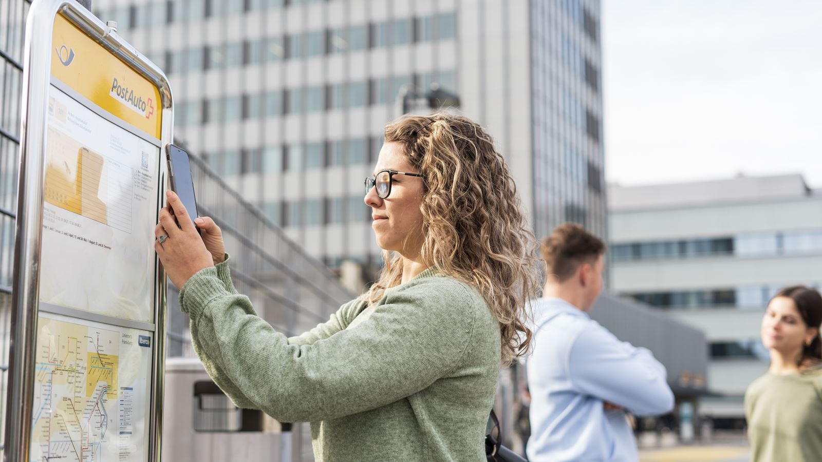 A woman scans the QR code for a timetable with her phone at a Postbus stop in Bern.
