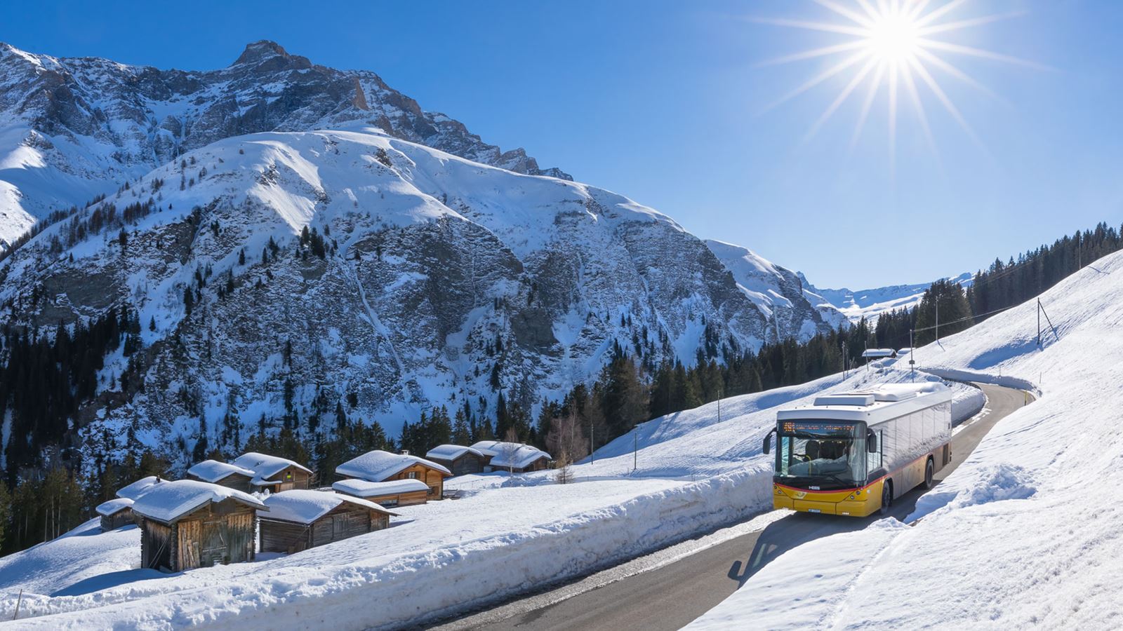 A Postbus drives through a snow-covered valley in Graubünden in beautiful winter weather.